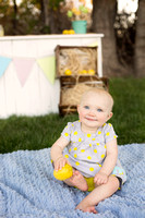 Baby girl holding a lemon in front of a lemonade stand.