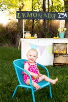 Baby girl's first birthday photo in front of lemonade stand.
