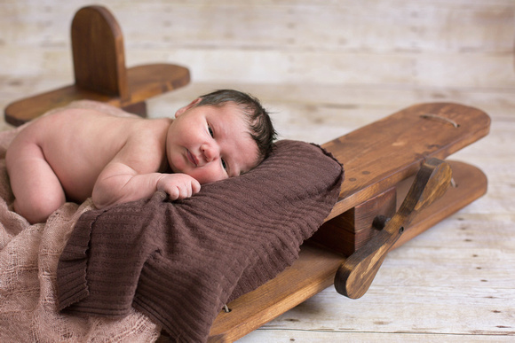 Newborn photograph of baby boy resting on a wooden airplane prop.