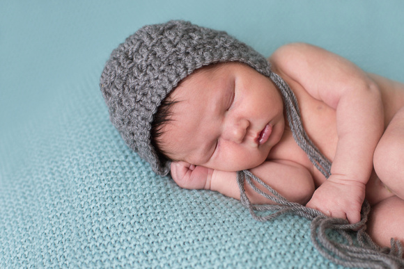 Sleeping newborn boy wearing a grey hat.